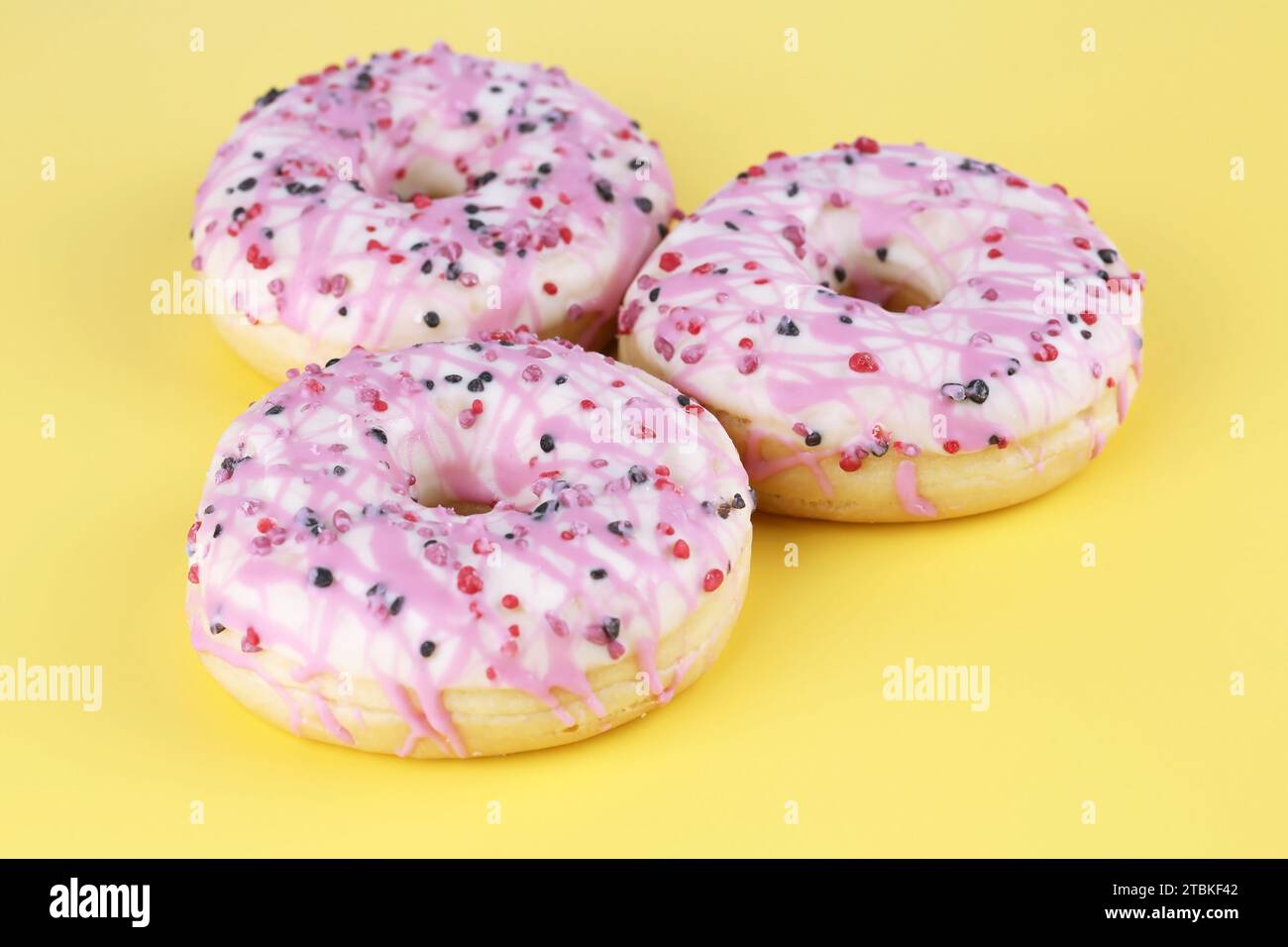 Three fresh colorful donuts on yellow background. Stock Photo