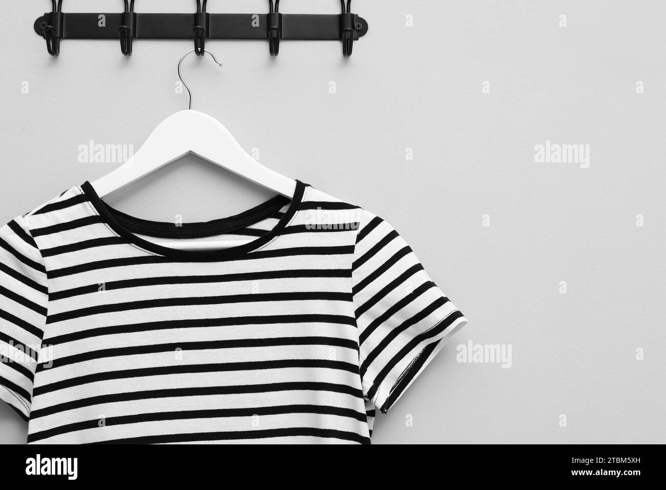 Hanger with striped T-shirt on light grey wall, space for text Stock Photo