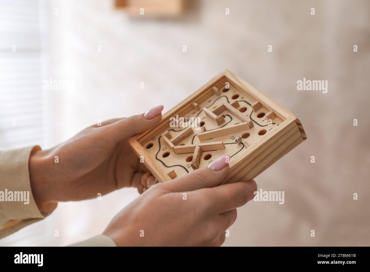 Woman holding wooden toy maze with metal ball on blurred background, closeup Stock Photo