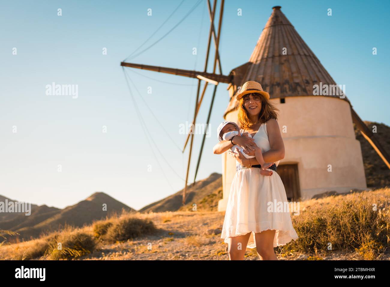 Mother holding a newborn baby next to a windmill in Cabo de Gata, Spain Stock Photo