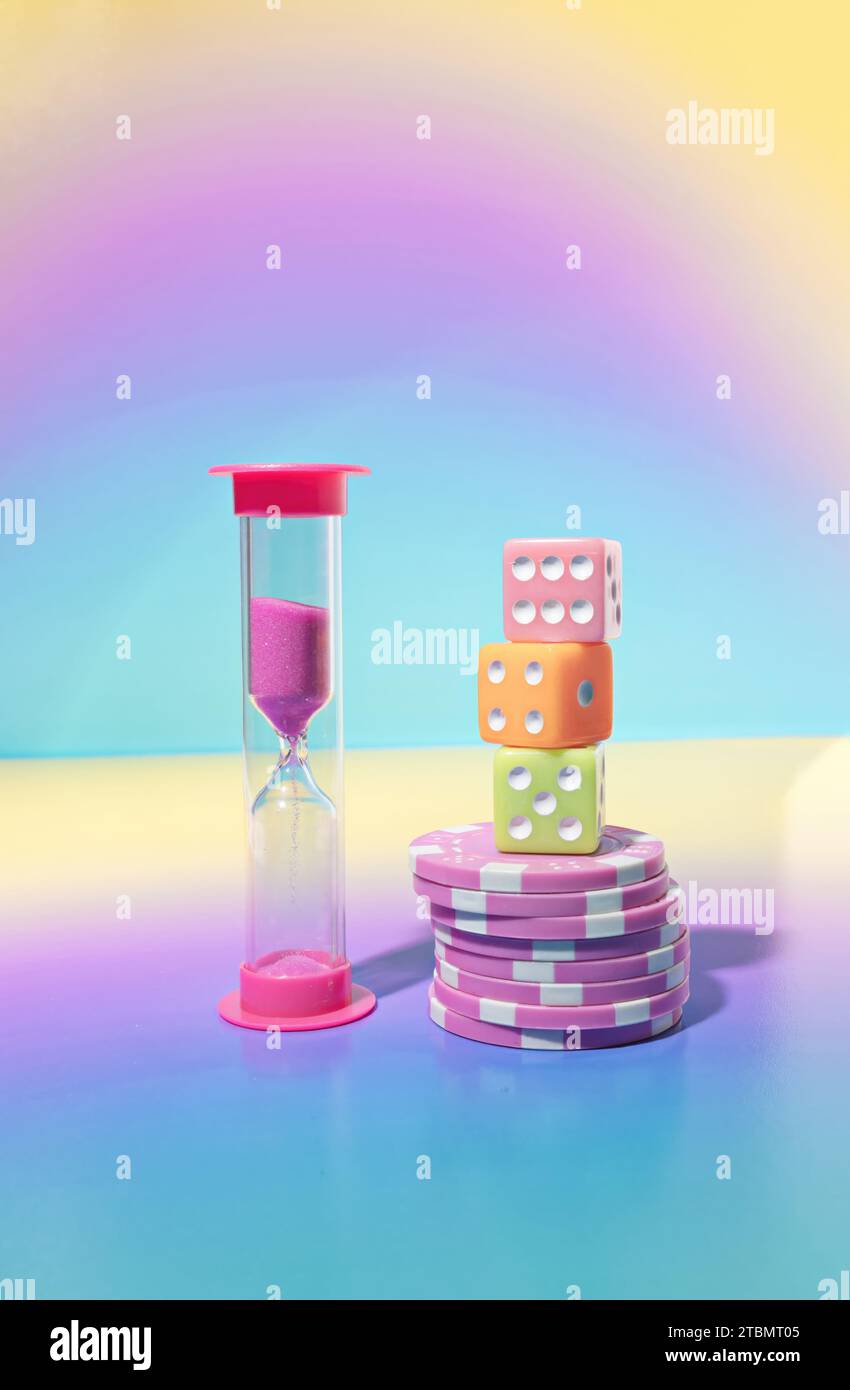 Game Night Scene, A Pink Sand Timer, Dice and Stacked Poker chips on a Pastel Gradient Background Stock Photo