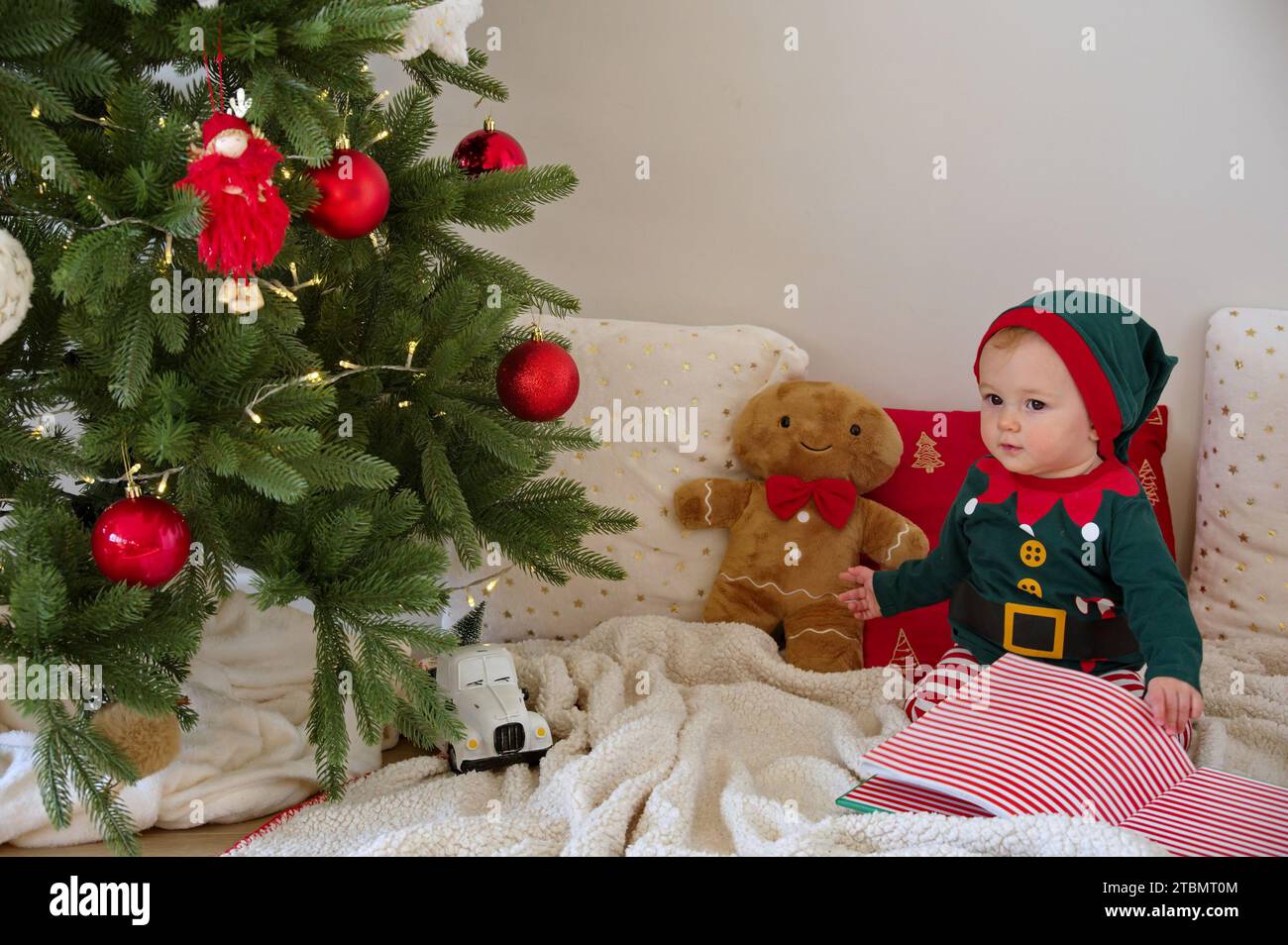 Baby girl dressed as elf sitting in front of Christmas tree Stock Photo