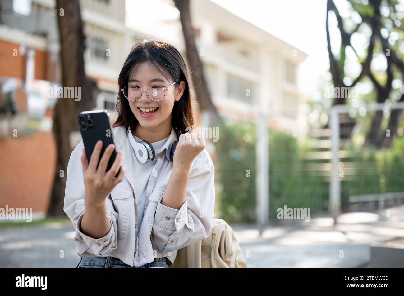 A cheerful and excited young Asian woman is looking at her smartphone ...
