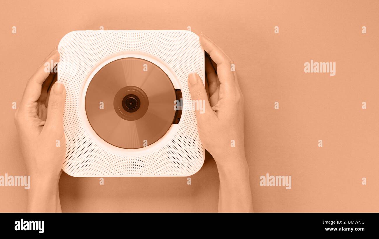 Hands holding stylish white compact CD player. Image toned in Peach Fuzz color of the year 2024. Retro vintage trending disc player. Top view, space Stock Photo