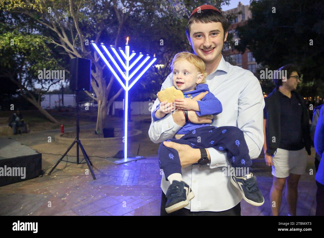 Shalom Kapuler, programming associate with ASU Chabad holds his son during the second annual Menorah lighting ceremony at Ragsdale-MLK Park in Tempe, Arizona on December 7, 2023. On the first night of Hanukkah, families engage in the tradition of lighting the Menorah which is a symbolic eight-branched candelabrum. (Photo By: Alexandra Buxbaum/Sipa USA) Credit: Sipa USA/Alamy Live News Stock Photo