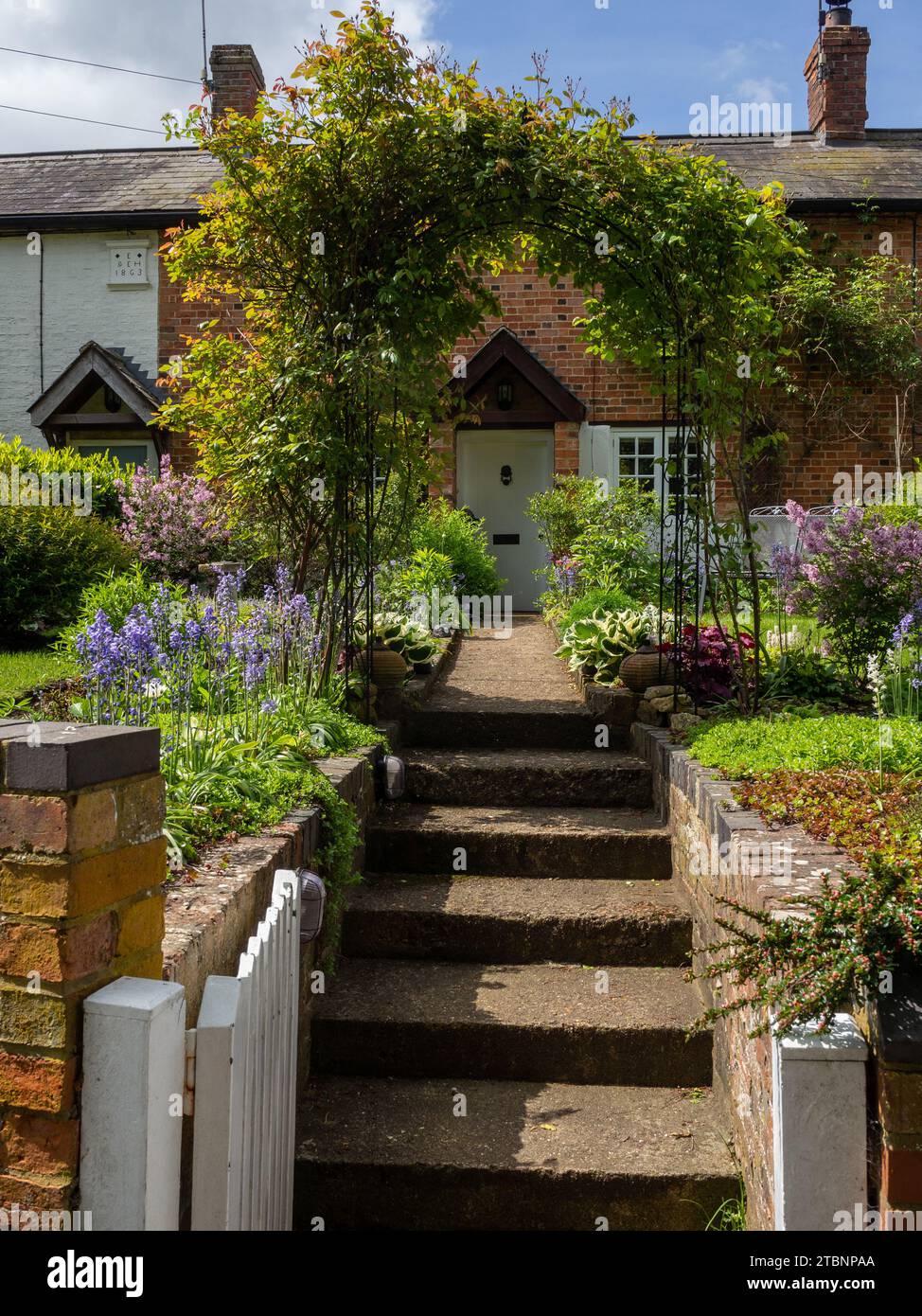 Open front gate with steps and path leading through an arbour to an old cottage, Abthorpe village, Northamptonshire, UK Stock Photo