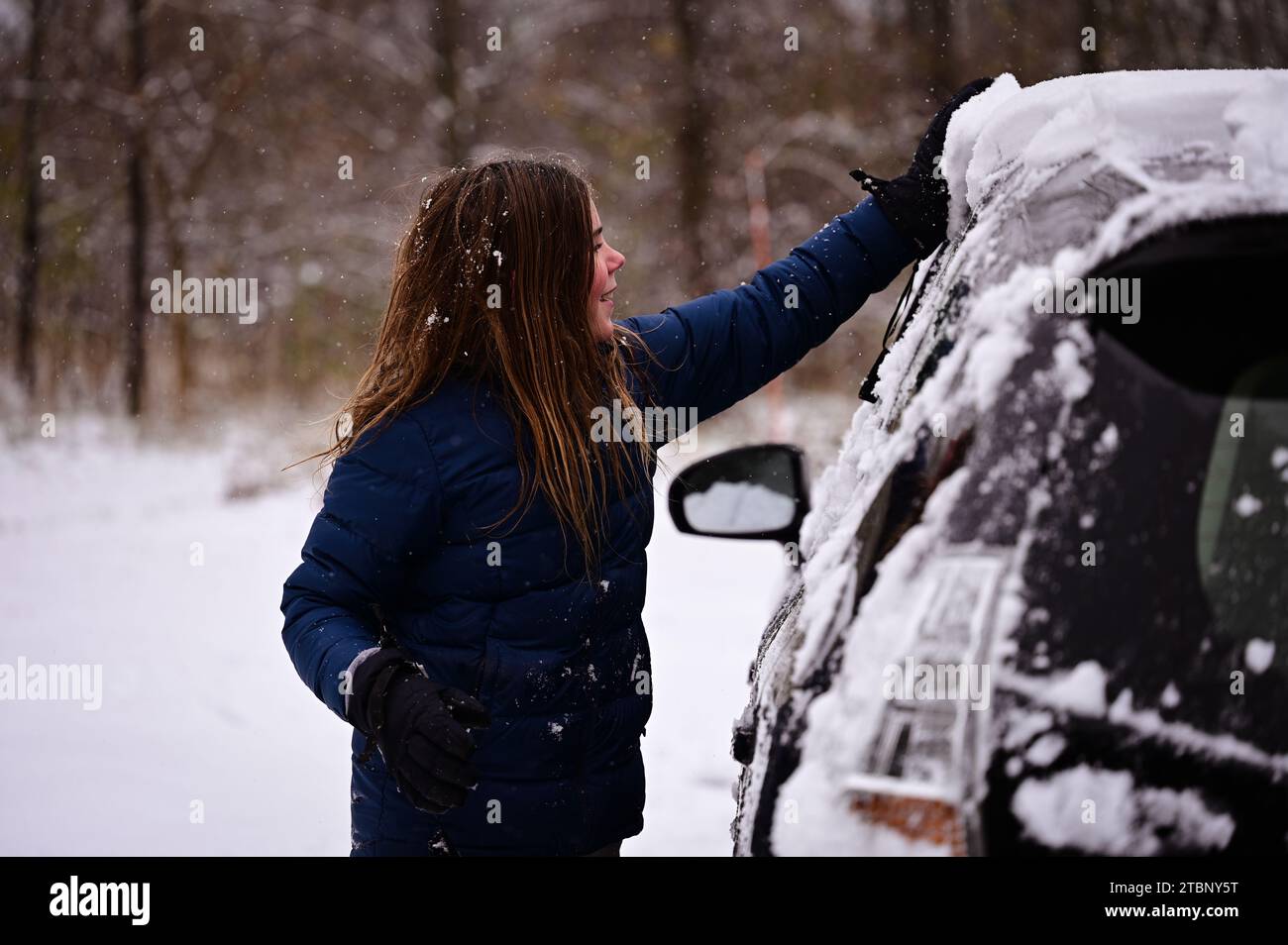 Smiling tween boy clearing snow from on top of car in winter Stock Photo