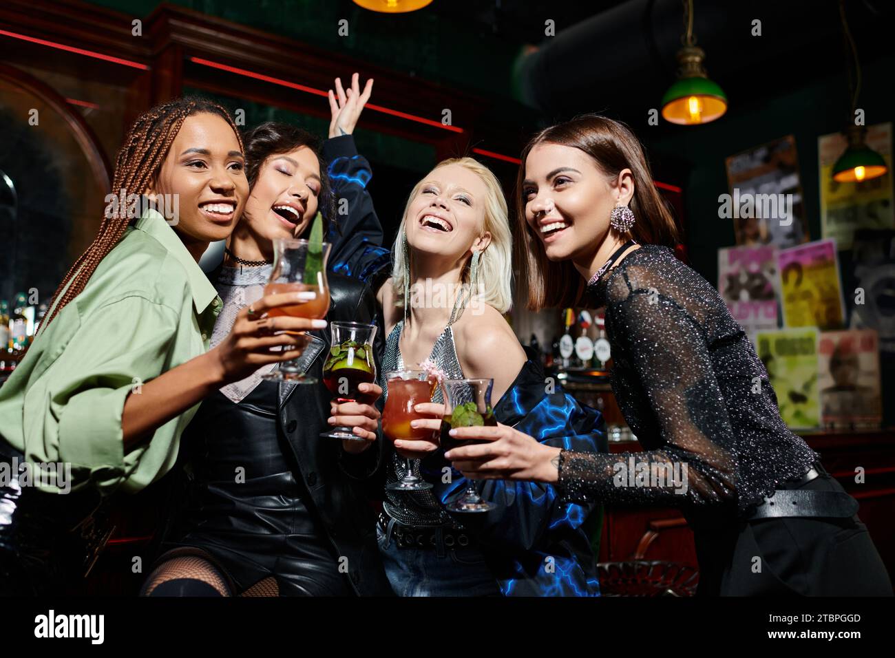 cheerful multiethnic fashionistas with delicious cocktails having fun in bar, vibrant atmosphere Stock Photo