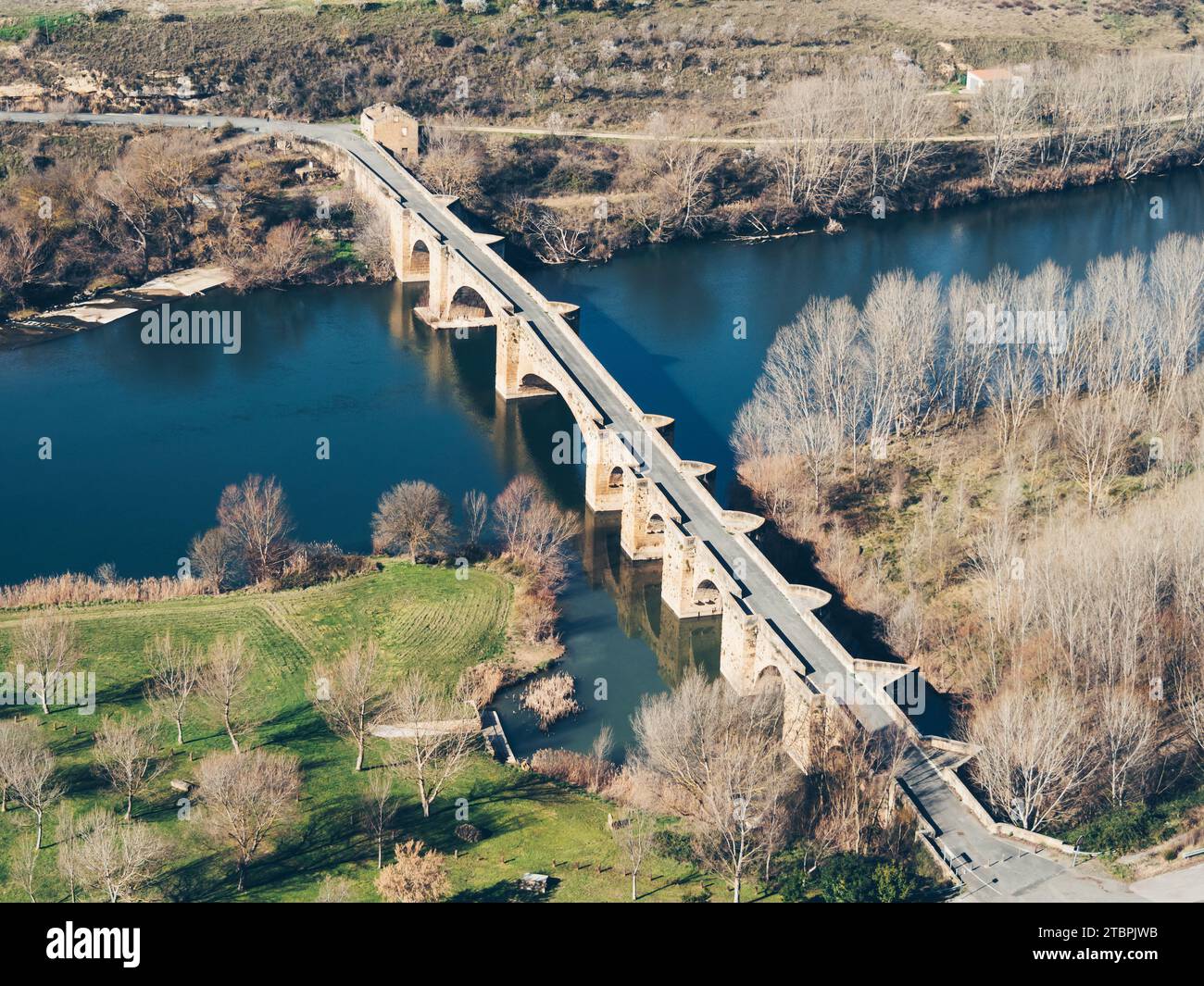 A train moves across a bridge spanning a river surrounded by natural mountain scenery in the background Stock Photo