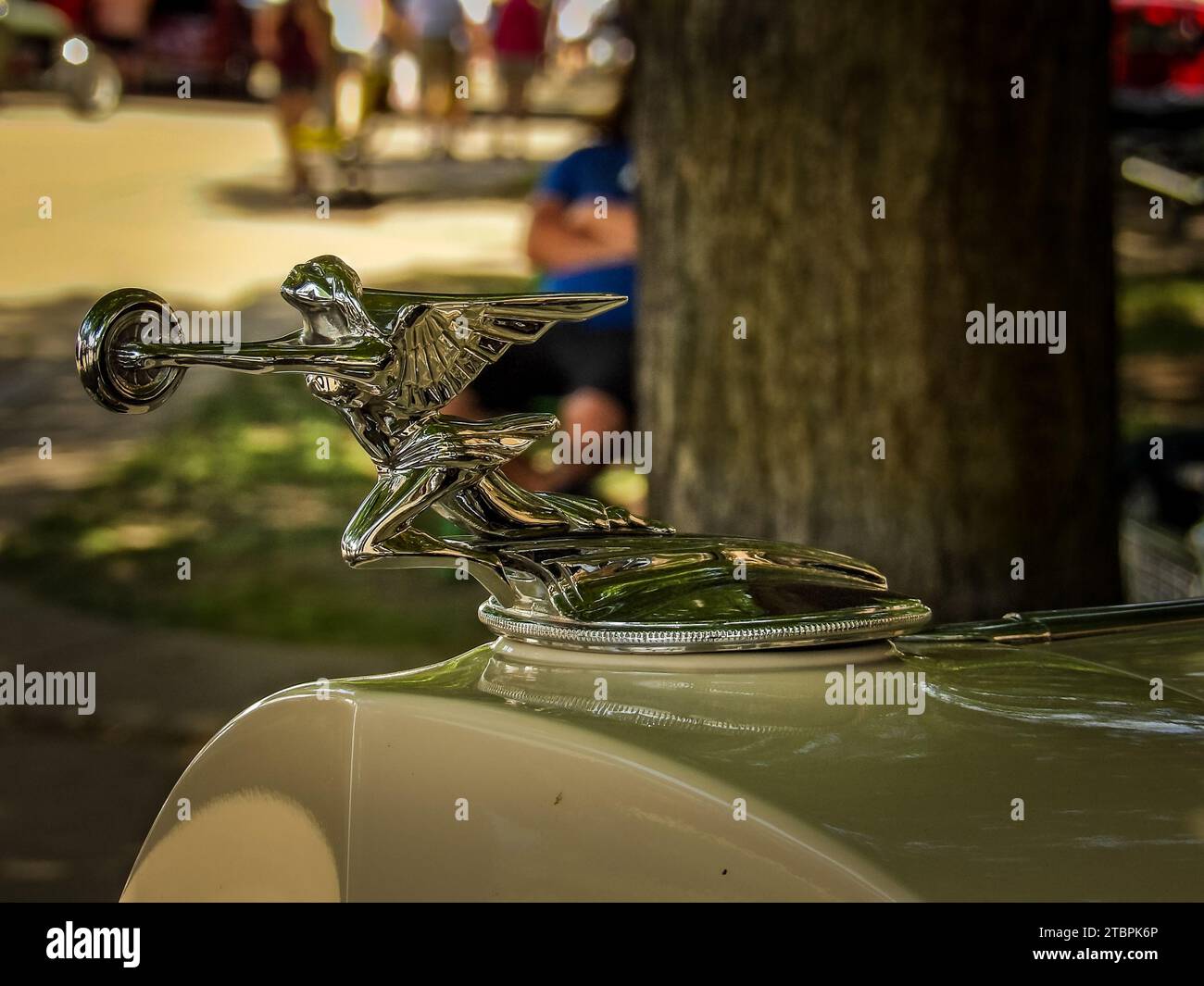 A vintage automobile hood ornament is displayed on the pavement next to a street curb Stock Photo