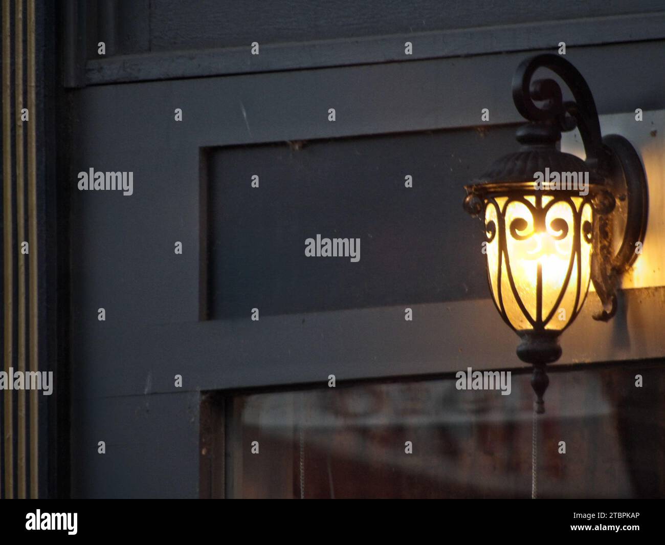A modern light fixture is illuminated on an exterior wall of an urban building, emitting a warm, inviting glow Stock Photo