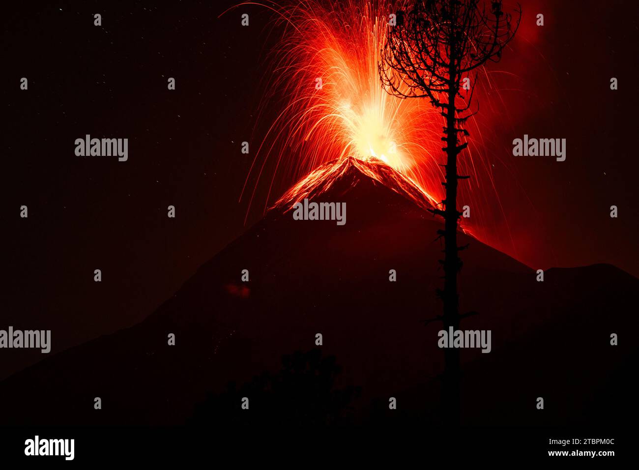 A scenic nighttime image featuring an active volcano with red lights illuminating it from below Stock Photo