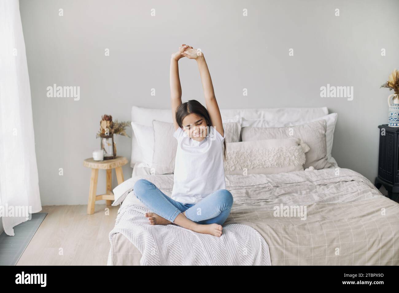 Preteen girl in casual clothes do stretching exercises seated on bed