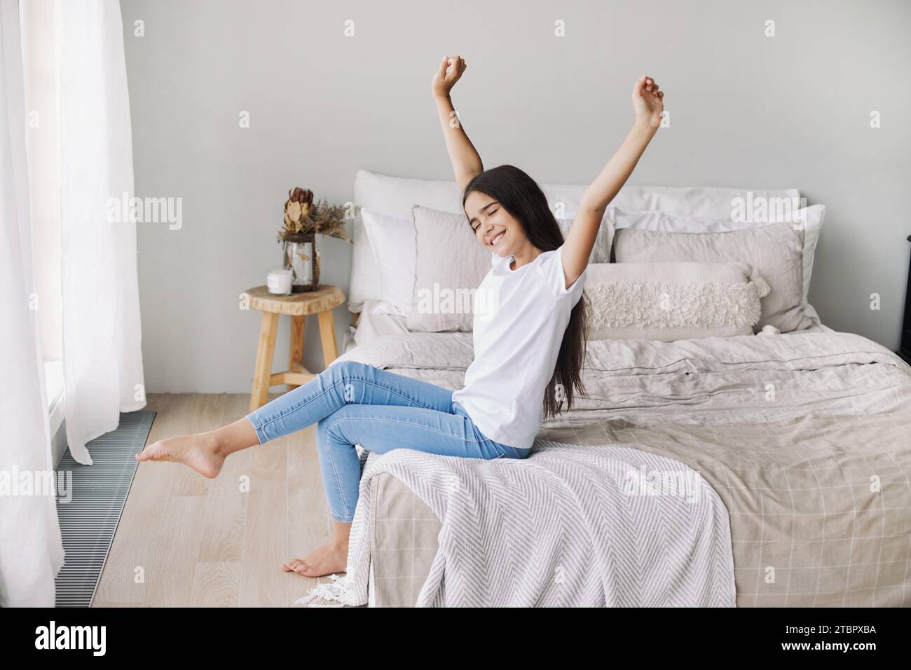 Preteen girl in casual clothes do stretching exercises seated on bed