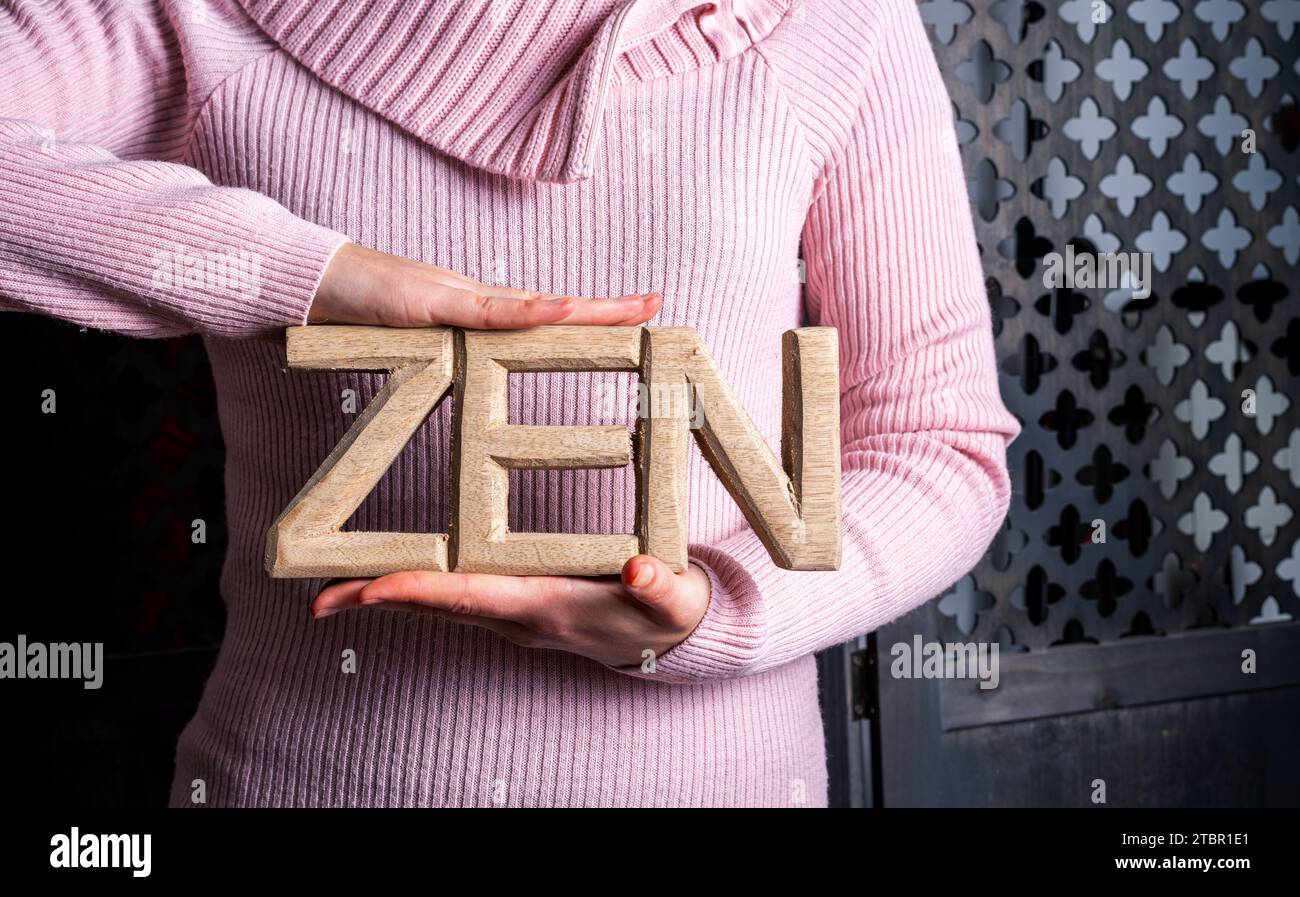 young woman in a pink pullover holding the word zen ,concept of wellbeing and healthy lifestyle . Stock Photo