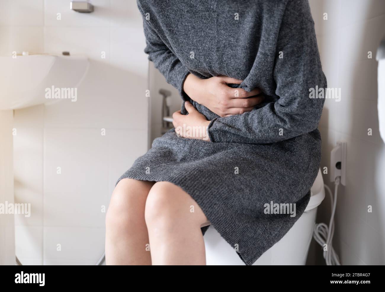 A woman suffering from stomach pain is sitting on the toilet and clutching her stomach Stock Photo