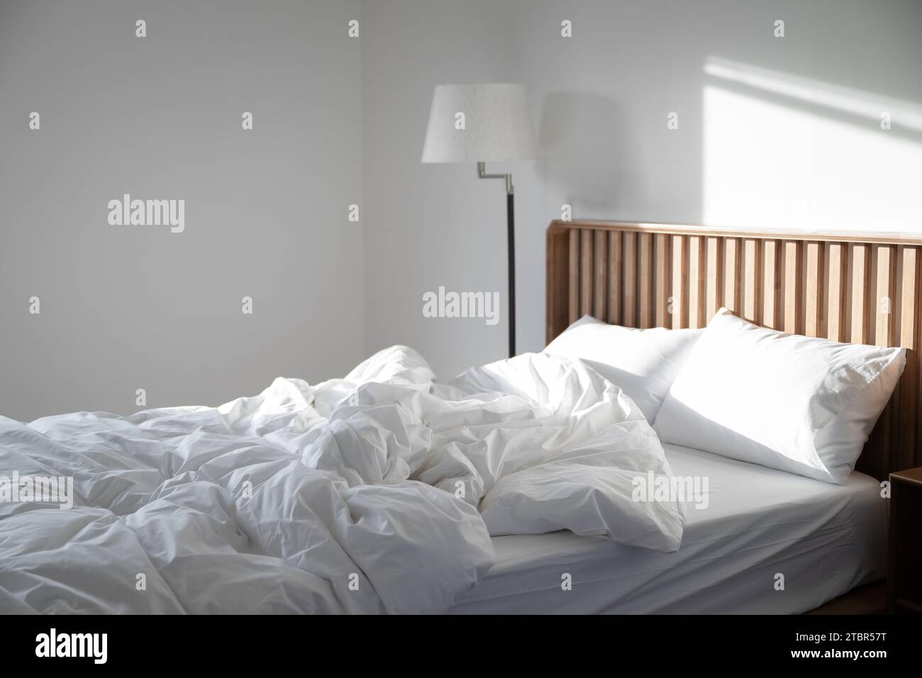 Sunlight falls on an empty room with untidy bedding Stock Photo