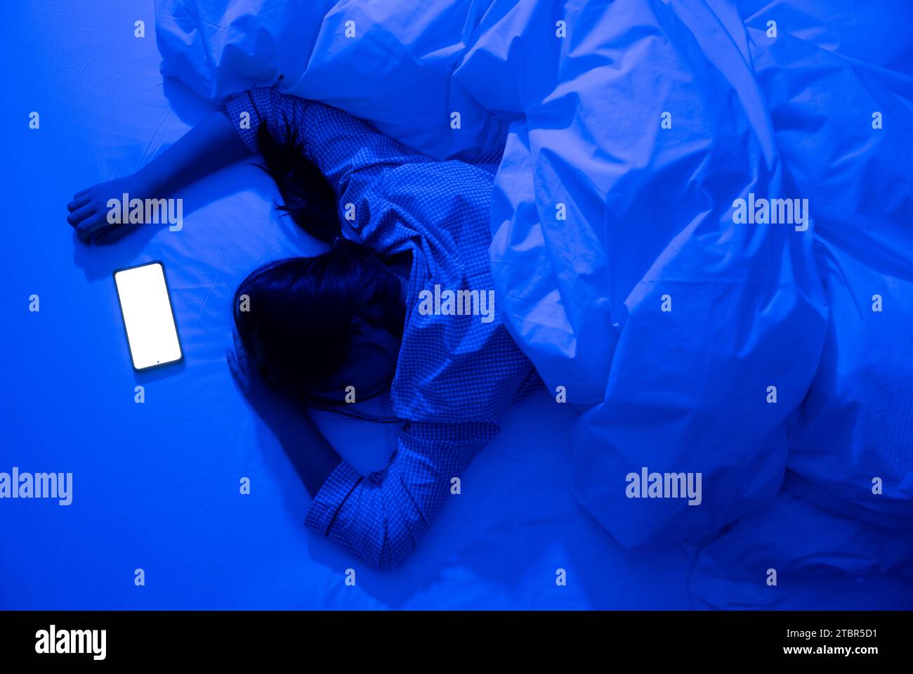 Woman using smartphone lying on bed late at night in bedroom with blue moonlight Stock Photo