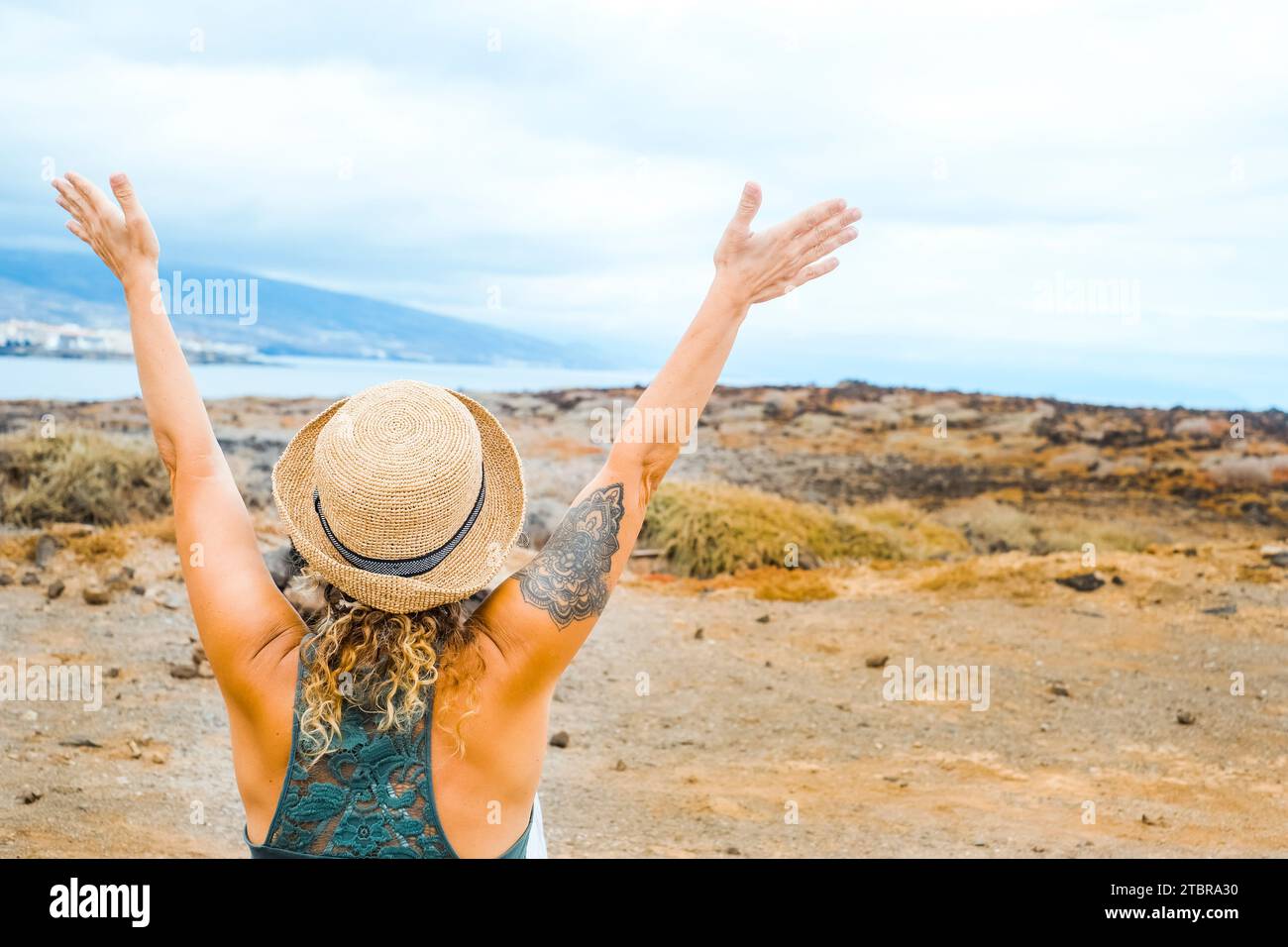 Back view of tourist woman raising up arms and enjoy excited the destination. Travel people lifestyle. Adventure journey female people happy and joy. Outdoor leisure activity people. Coastline and sky Stock Photo