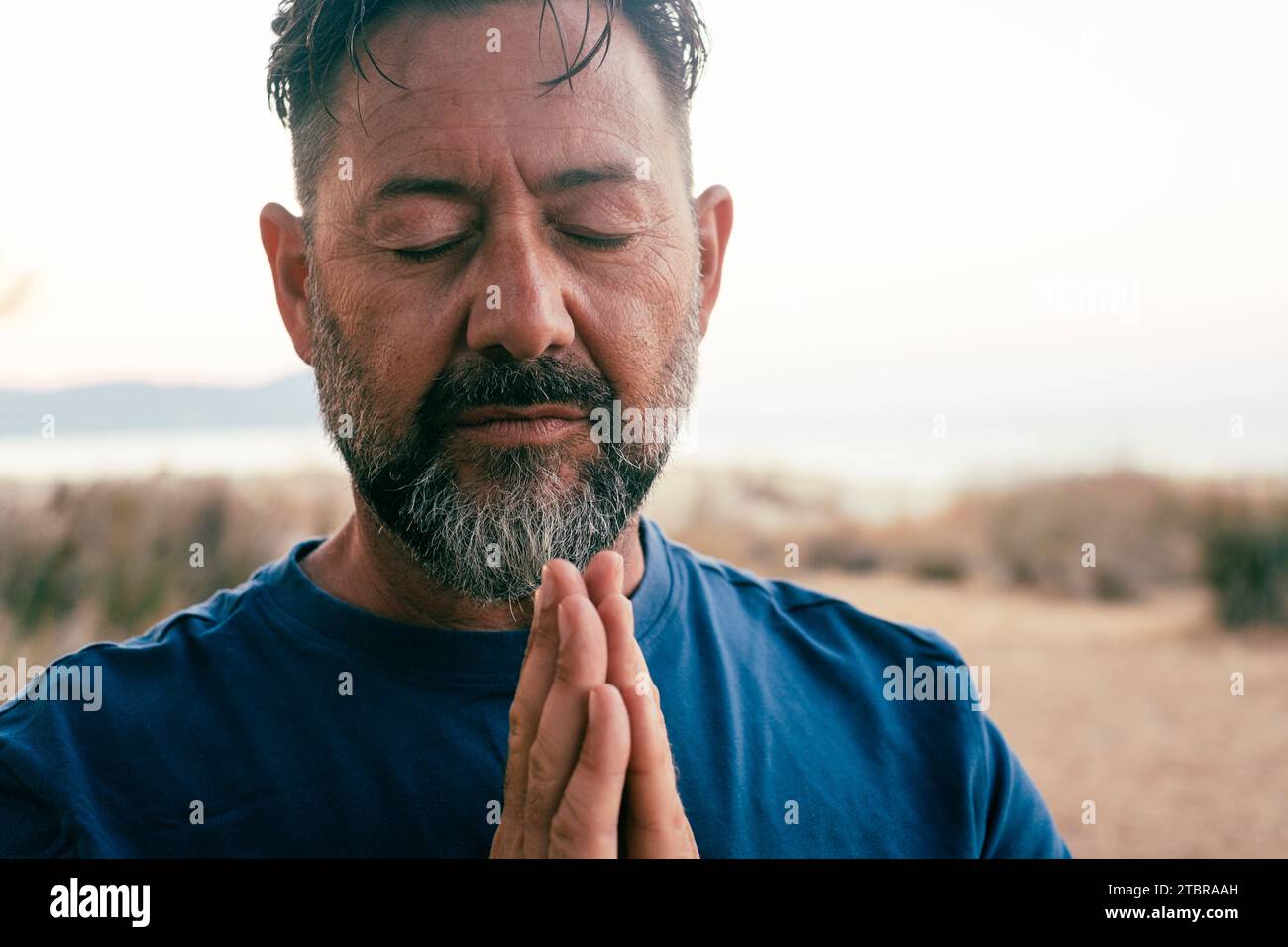 One adult man praying and meditate outdoor in relaxation gesture with hands clasped and closed eyes portrait. Zen like healthy mental balance lifestyle male people. Wellbeing. People zen exercise Stock Photo
