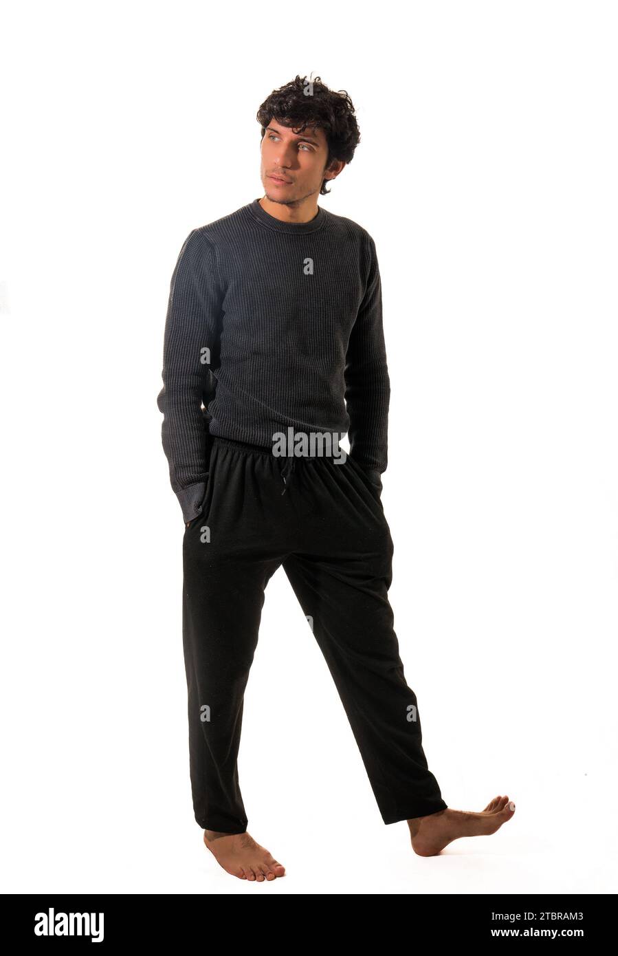 A man in a black sweater and black pants, walking around, with hands in pockets, full figure shot isolated on white Stock Photo