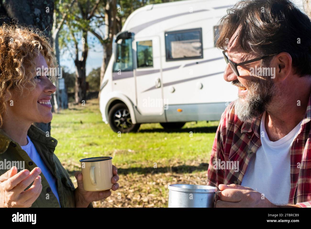 Happy couple of traveler tourist enjoy relax and drinking coffee during travel pause in outdoor at the park with modern rv motorhome vehicle in background under the trees. Autumn journey adventure Stock Photo