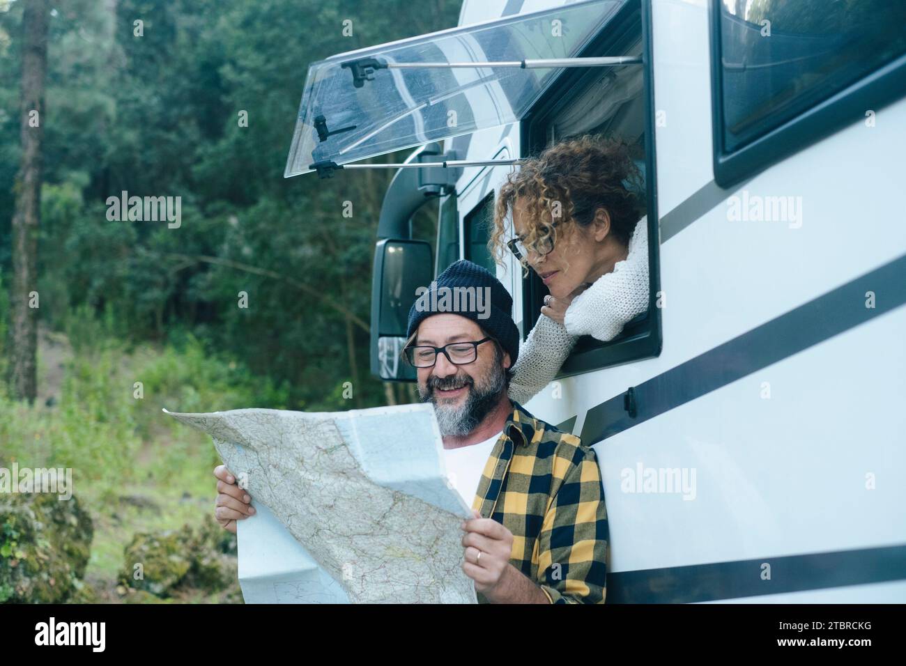 Happy traveler couple adult man and woman looking together a map guide to choose next destination. Vanlife and travel adventure vacation with camper van motorhome modern vehicle lifestyle. Nature Stock Photo