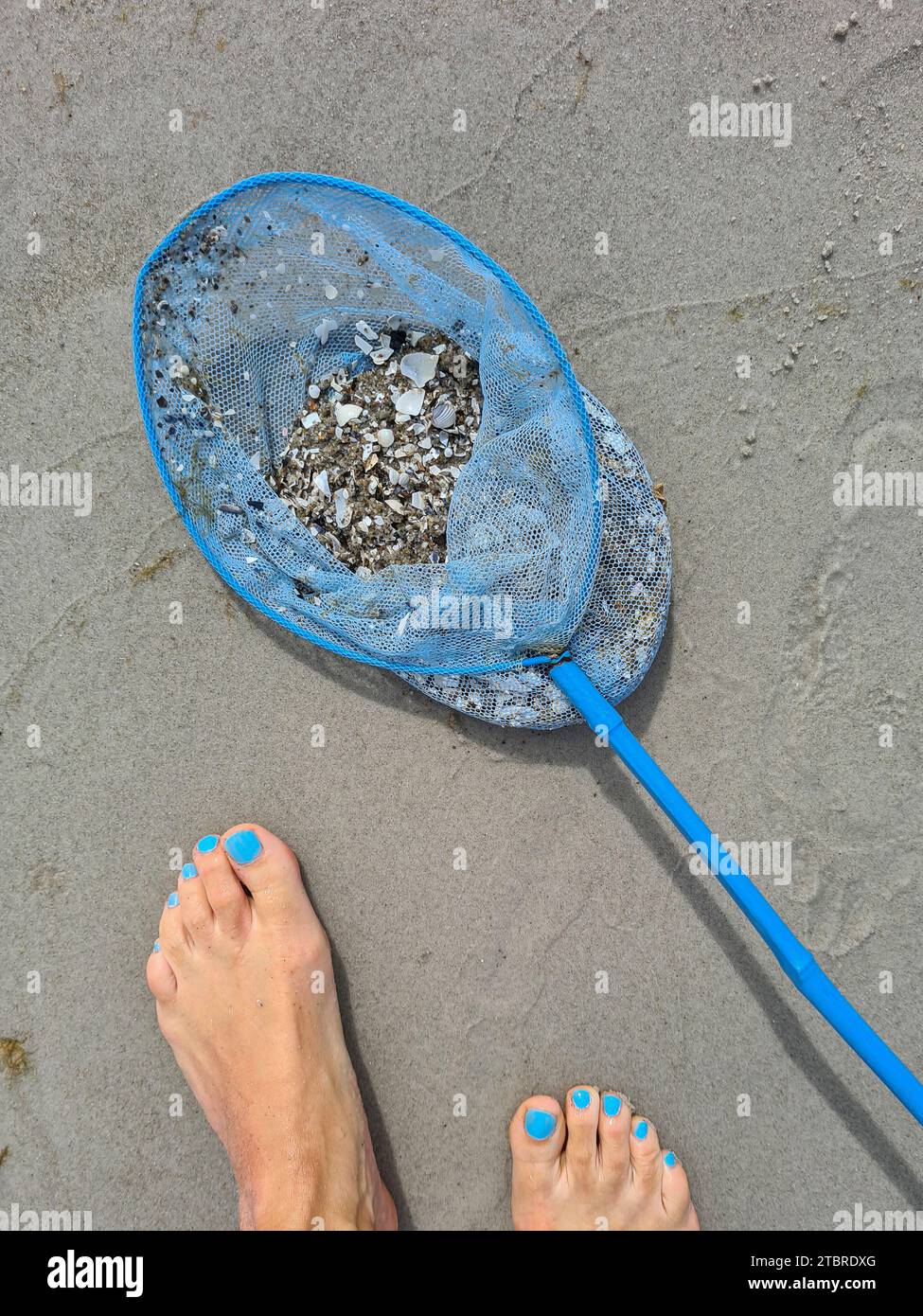 Germany, Mecklenburg-Western Pomerania, peninsula Fischland-Darß-Zingst, blue landing net lies next to women feet on the sandy beach of Prerow Stock Photo