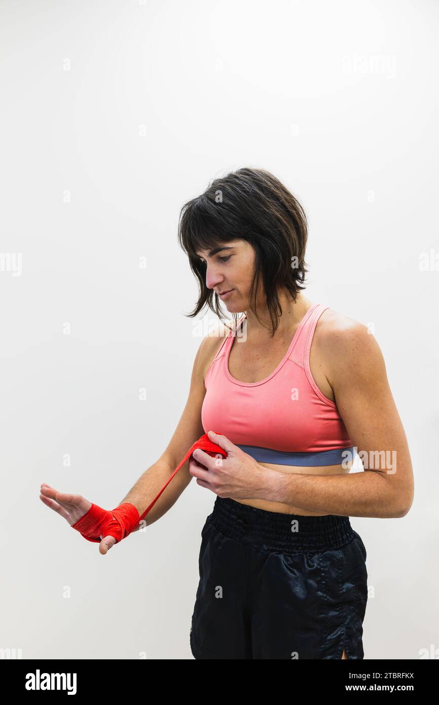 Vertical photo woman mid adult caucasian standing, putting red bandages on her hands for boxing, on white copy space background. Sports and recreation Stock Photo
