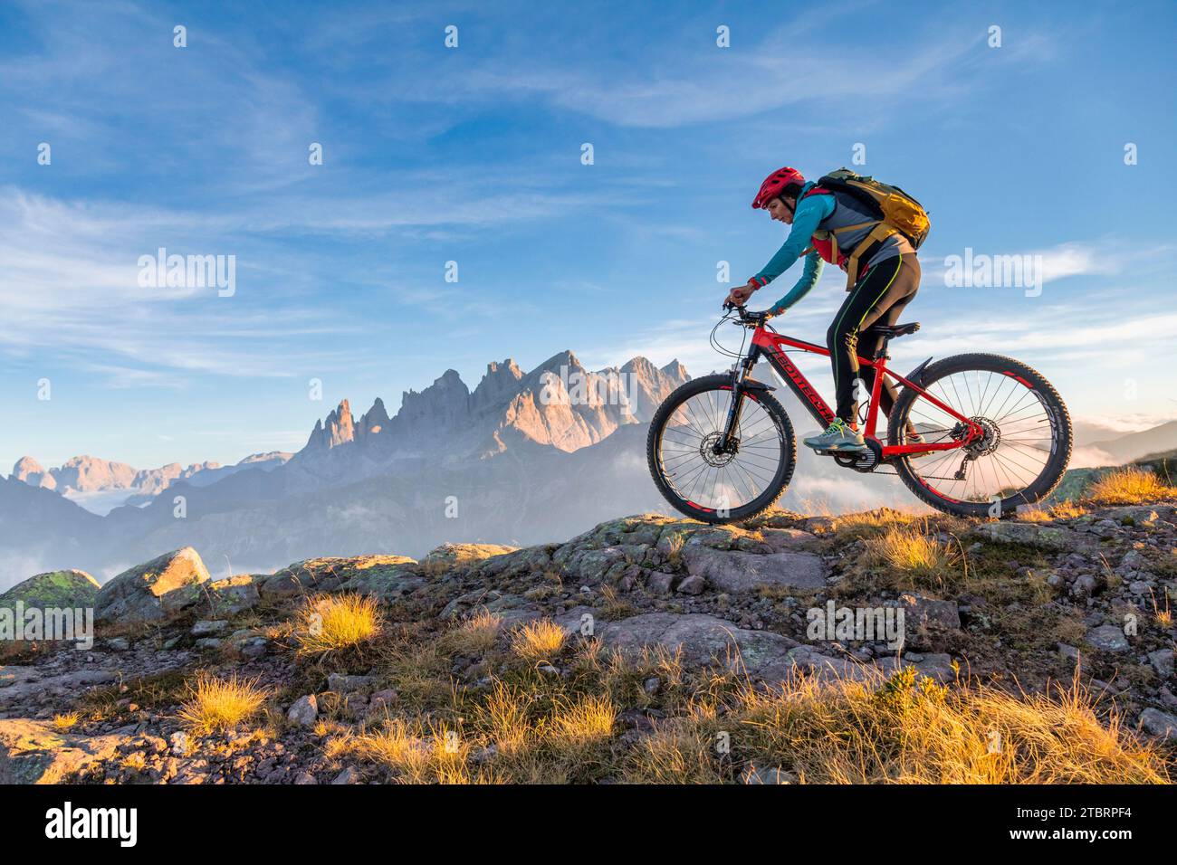 Italy, Veneto, province of Belluno, Falcade, outdoor activities with family, woman cyclist riding an e-bike in the mountains, in the background the Pale di San Martino chain at sunset Stock Photo