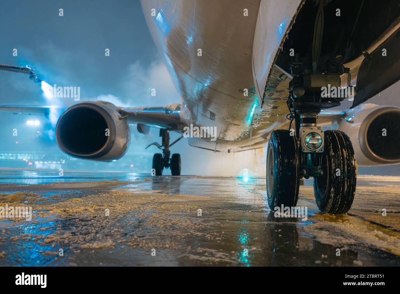 Selective focus on landing gear of airplane during deicing before take off. Winter frosty night and ground service at airport. Stock Photo