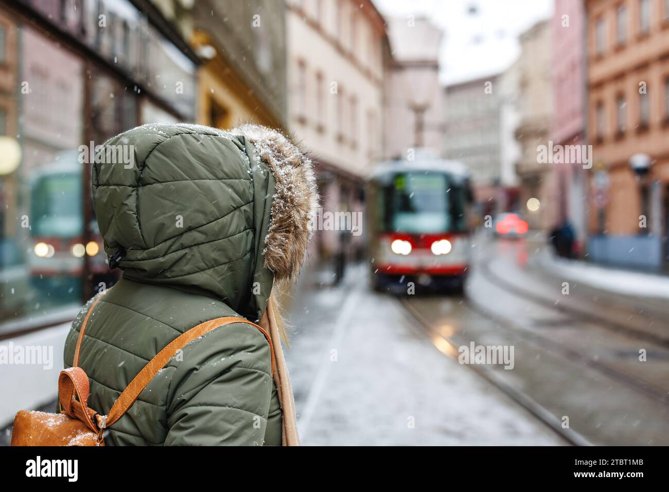 Public transport in the city during snowfall. Woman with winter coat is waiting for tram on street Stock Photo