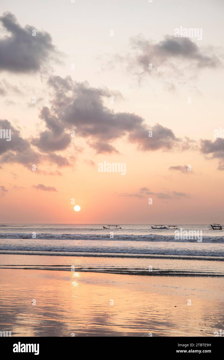 Dreamlike sunset on the dream beach of Kuta, small waves in the sea and the reflection of the sky in the shallow water, tropical Bali, Indonesia Stock Photo