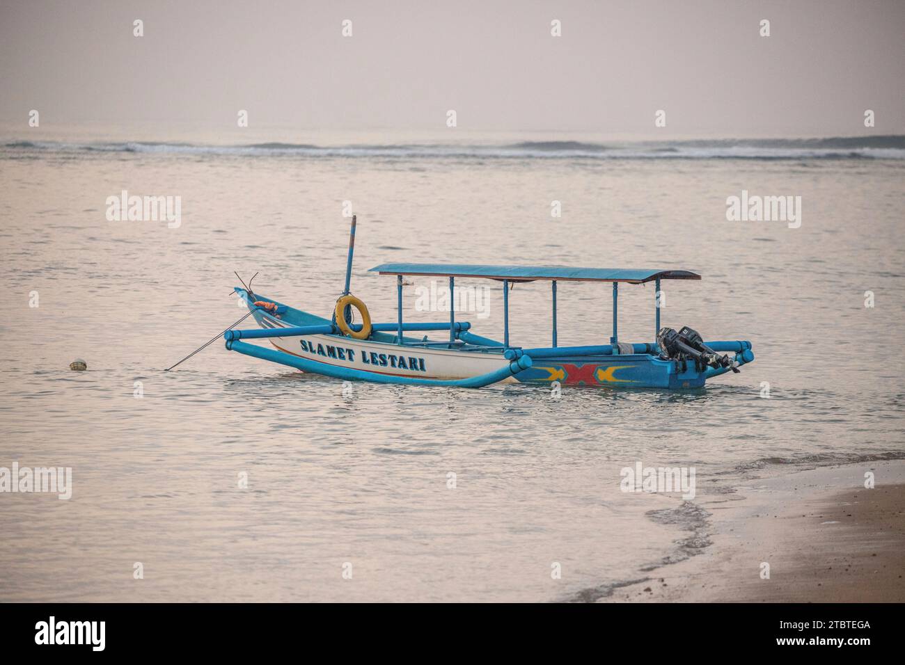 Morning landscape taken on a sandy beach, view over the sea to the horizon with small temples in the water and a jukung, a traditional fishing boat in the sea, sunrise in Sanur, Bali, Indonesia Stock Photo