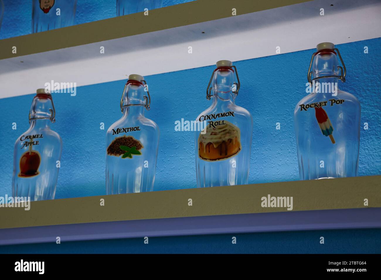 Eye-Level View of Flavored Glass Vape Bottles on Modern Shelf Against Blue Wall Stock Photo