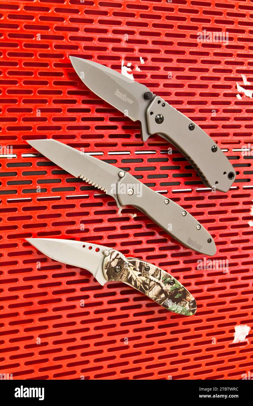 Organized Display of Folding Knives on Vibrant Red Pegboard Stock Photo