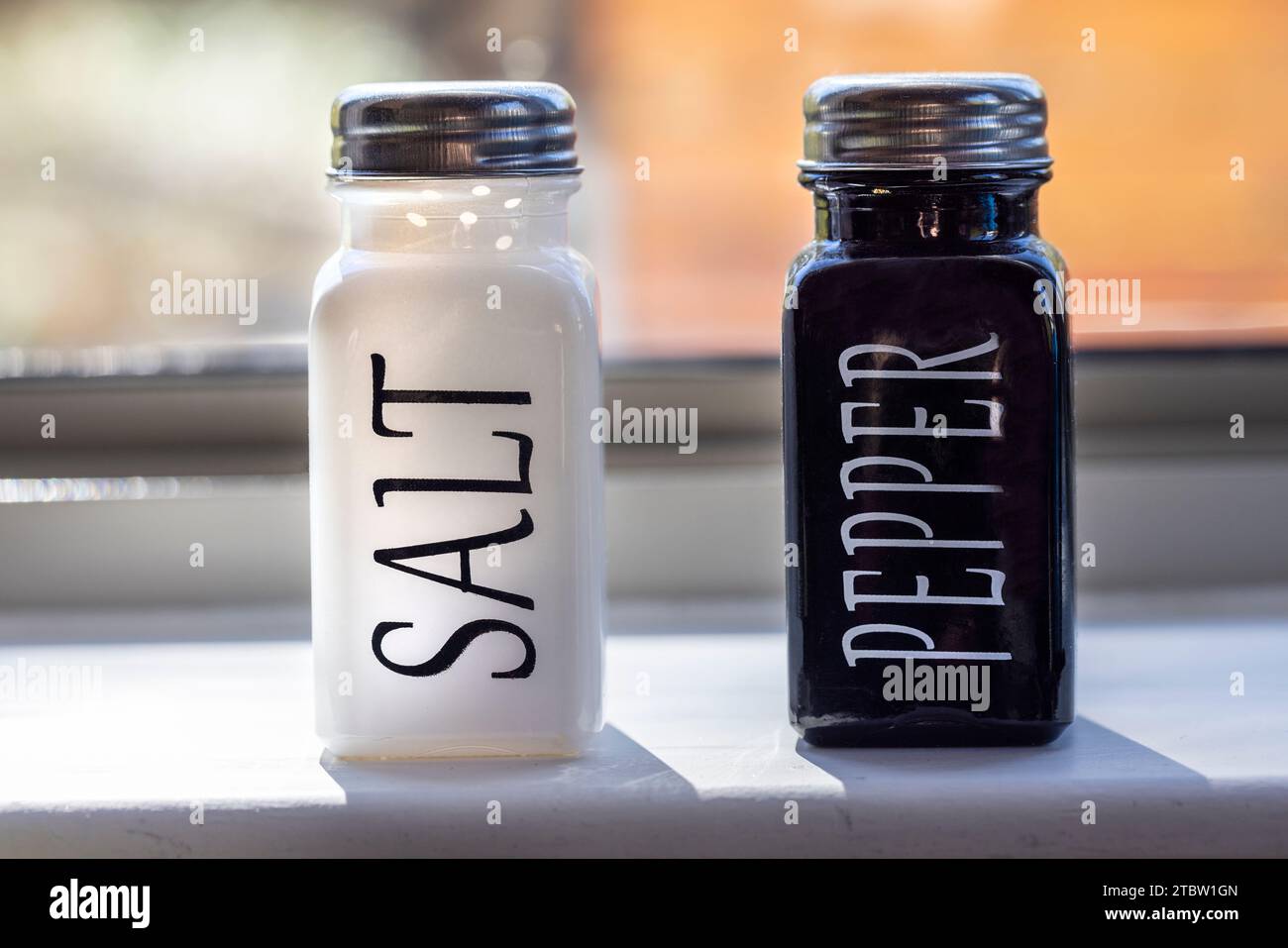 White and black ceramic bottles of salt and pepper with metal screw top lids Stock Photo