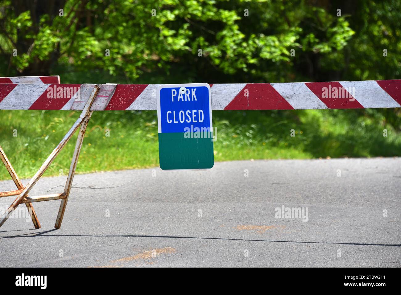 Barrier bars access to park area.  State park are closed due to spread of COVID 19 virus.  Barrier is red and white striped with a blue posted sign. Stock Photo