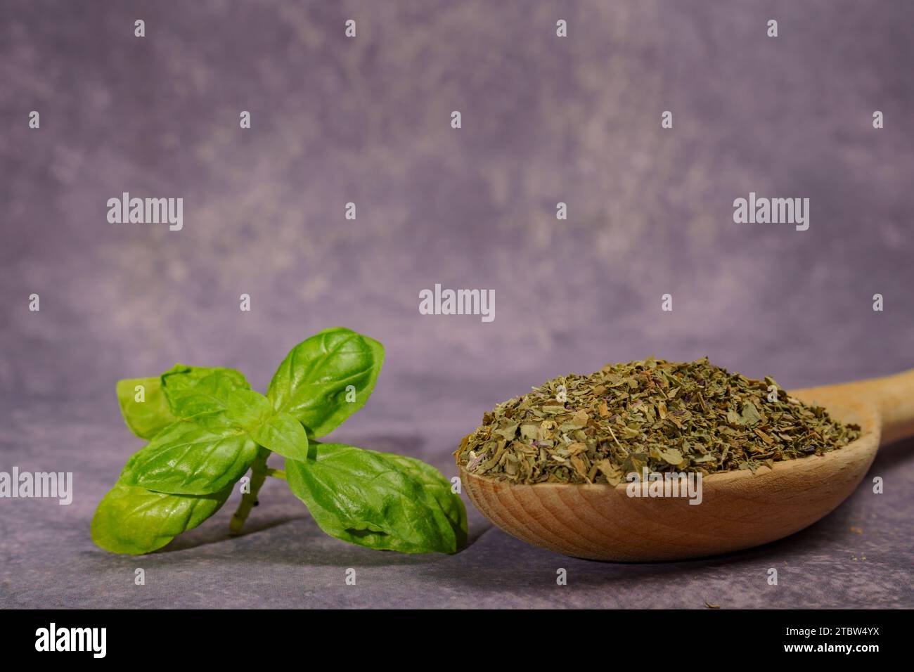 dried basil ground in a wooden spoon with freshly cut basil leaves Stock Photo