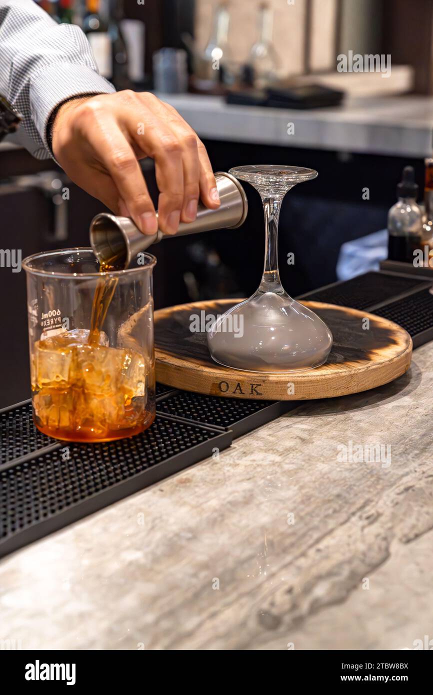 Bartender pouring whiskey out of a jigger and making smoked whiskey cocktail drink Stock Photo