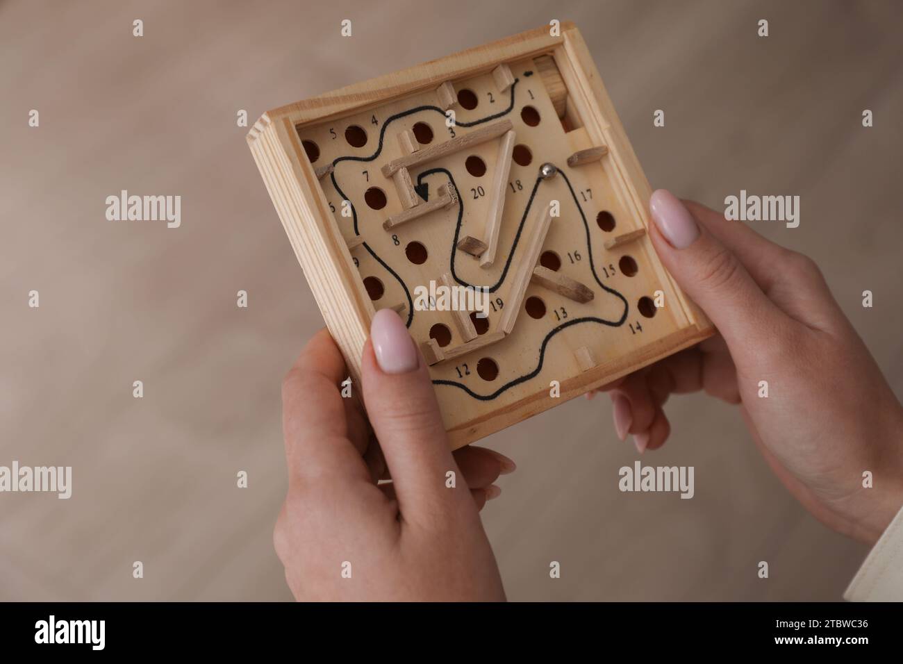 Woman holding wooden toy maze with metal ball on blurred background, closeup Stock Photo