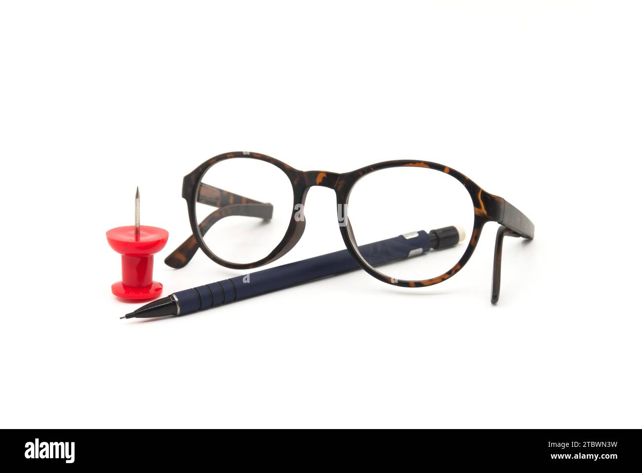 Reading glasses with tortoiseshell frames, pen and colorful red thumb tack over a white background with copy space in a business still life Stock Photo