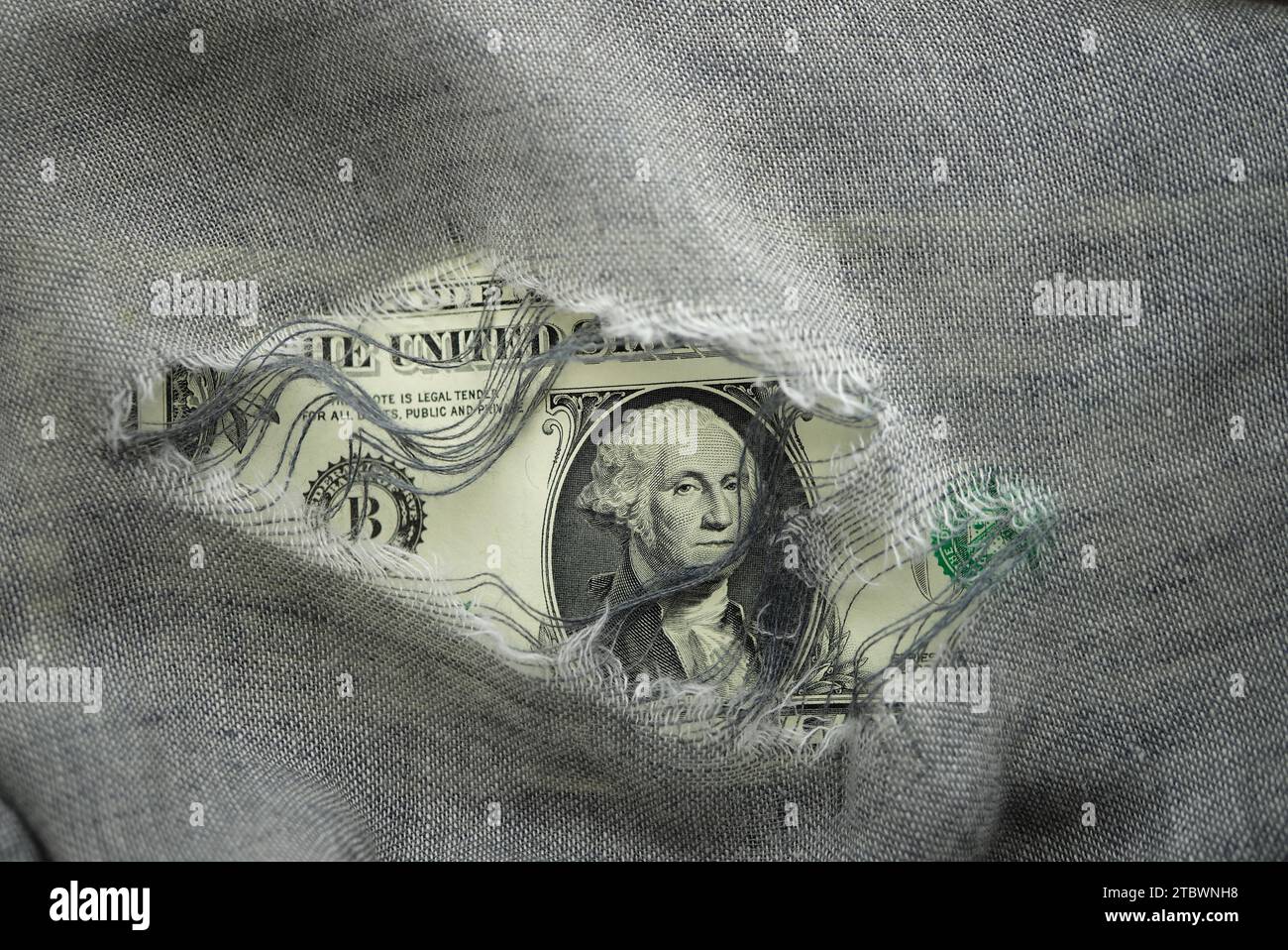 USD banknote viewed through a hole in torn grey fabric with focus to the portrait of Washington in a financial or economic concept Stock Photo
