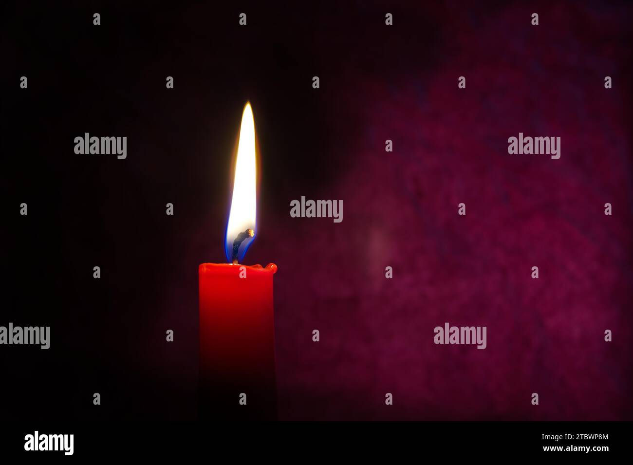 Single red candle burning alone in the dark red background. Conceptual image symbolize peace