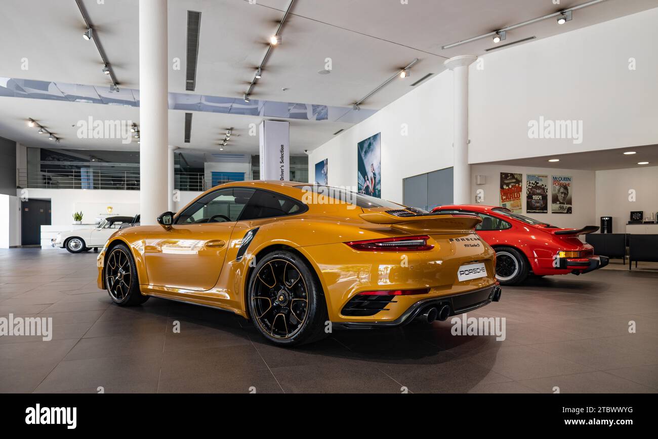 A picture of an orange Porsche 911 Turbo S next to a red Porsche 911 Carrera 3.0 inside a dealership Stock Photo