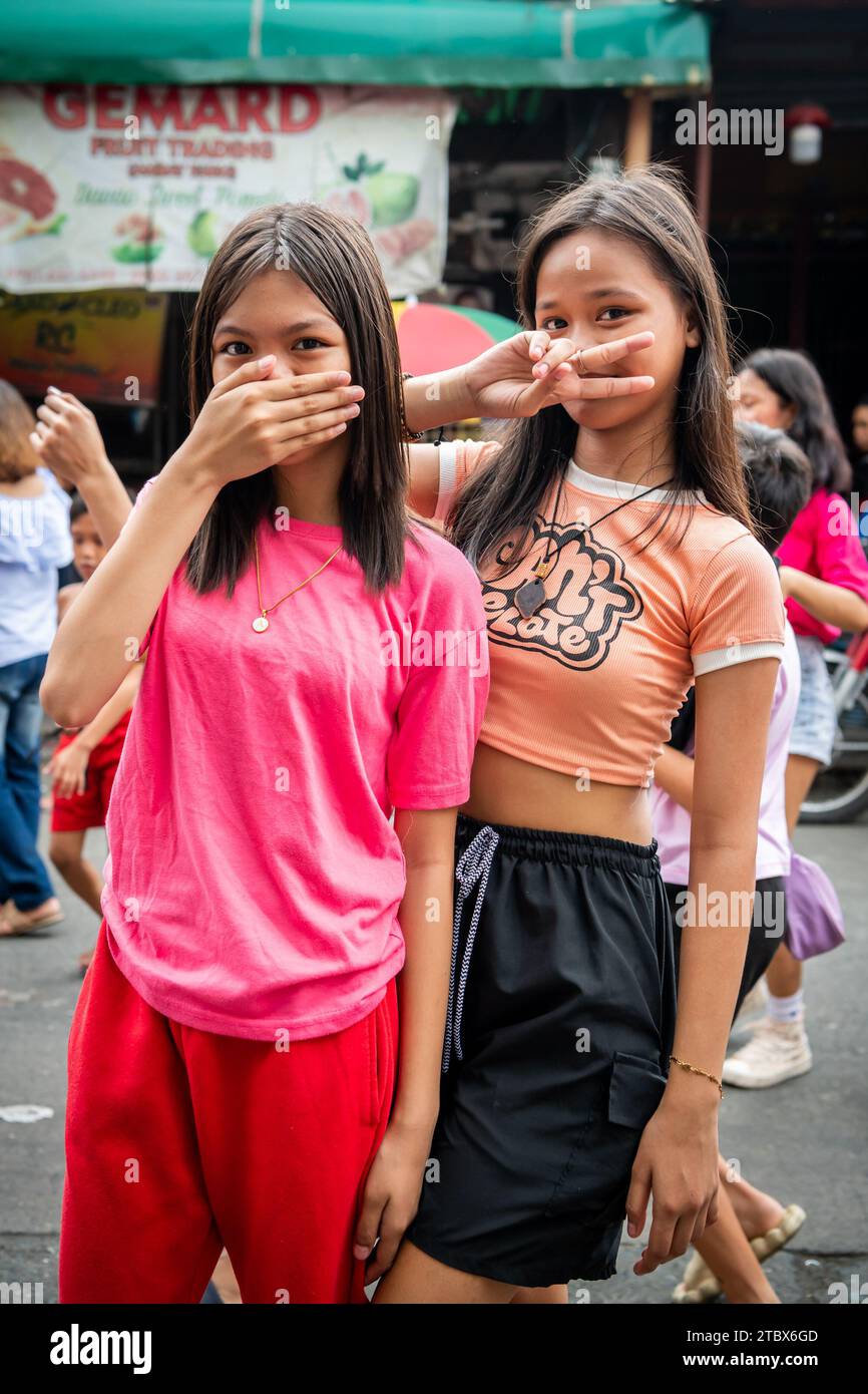 Two Young Filipino Girls Make A Cheeky Pose And Hand Signal During A Religious Festival In