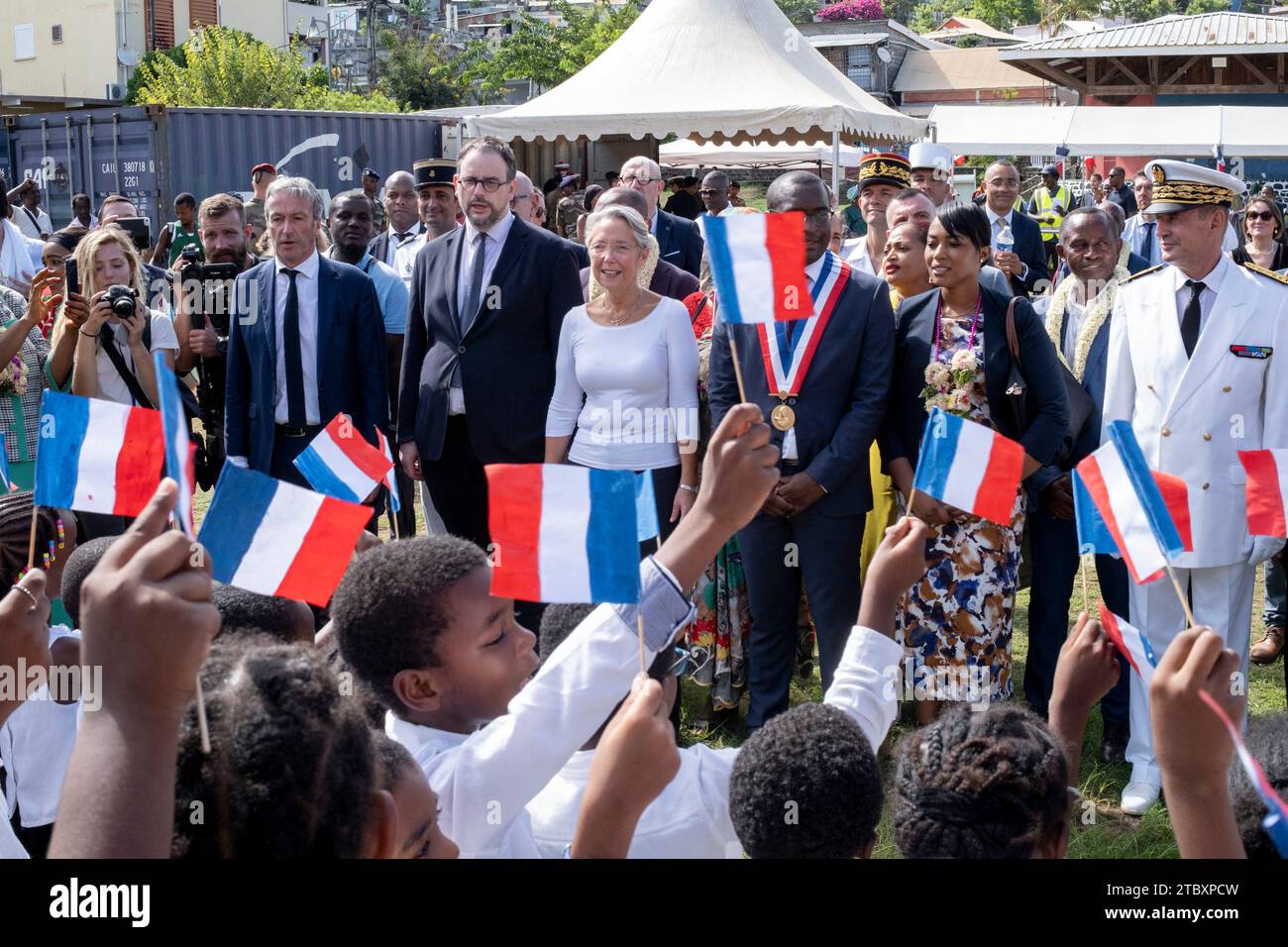 Children wave national flags and sing French national anthem upon the arrival of French Prime Minister Elisabteh Borne flanked by French Minister for Overseas Philippe Vigier and French Health Minister Aurelien Rousseau to visit a local resident waiting for exchanging her empty bottles of water for filled ones in Labattoir in Dzaoudzi on the French Indian Ocean island of Mayotte, on December 8, 2023, for their one-day visit. French Prime Minister travels to Mayotte on December 8, 2023 to make announcements on water, housing and health in French poorest department, which faces severe drought, m Stock Photo