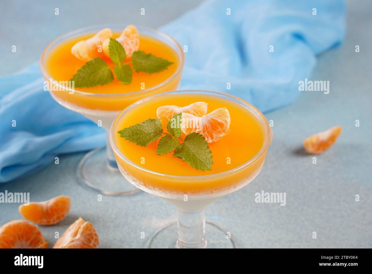 Vanilla panna cotta with tangerine layer in a small portioned vase and fruit pieces in wineglasses. Delicious Italian dessert. Stock Photo
