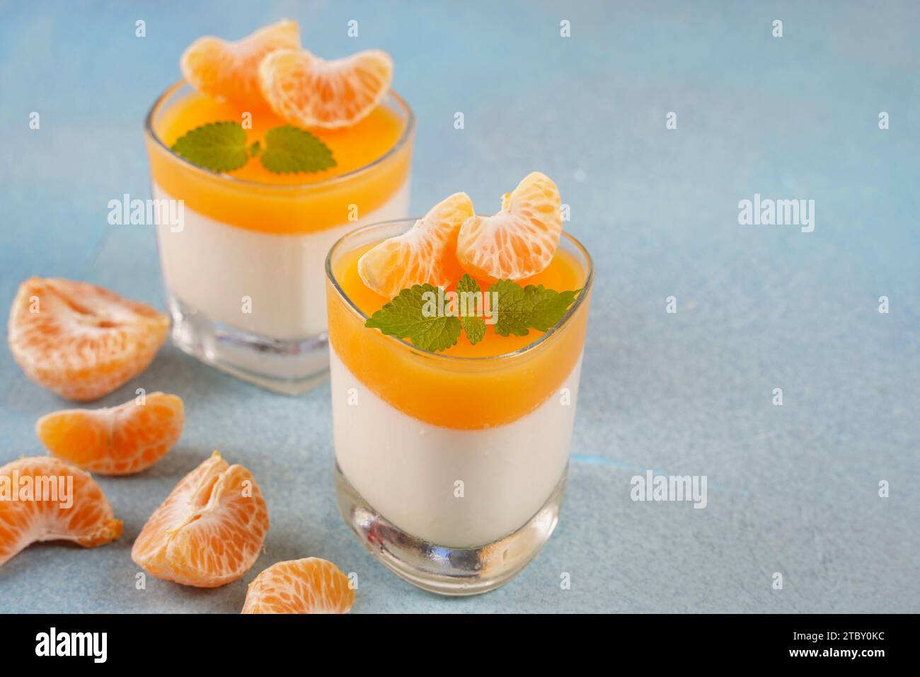 Vanilla panna cotta with tangerine layer in a small portioned vase and fruit pieces in wineglasses. Delicious Italian dessert. Stock Photo