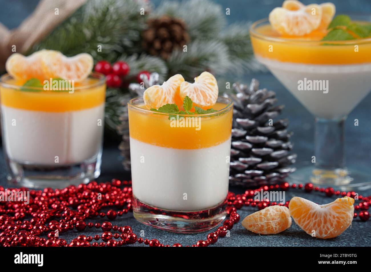 Panna cotta with tangerines jelly and mint, Italian dessert, homemade cuisine. On the background are branches of a green Christmas tree. Stock Photo